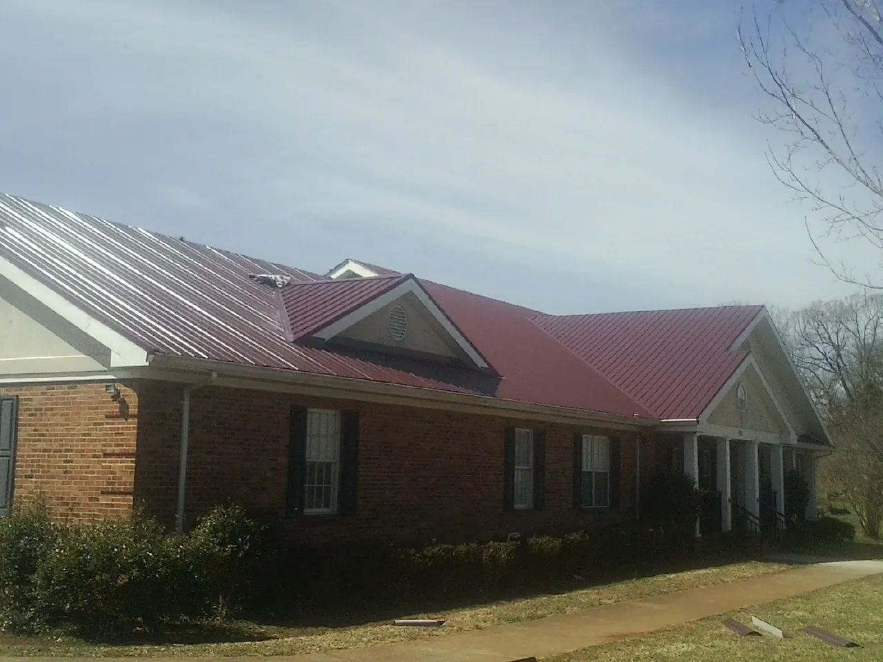 Red metal roof with gabled entries on a long brick building, from a Hail Damage Roof Repair job in North Salem