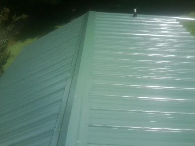 New green metal panels meeting at the ridge of a roof — Flat Roof Repair work by our crew in North Salem