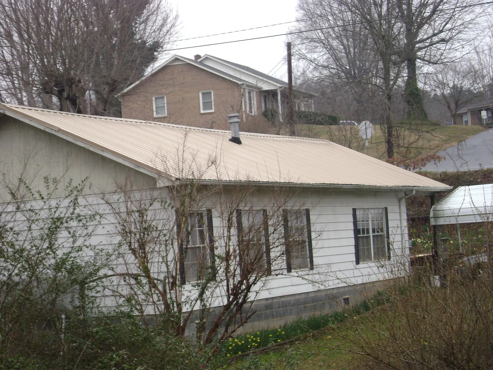 Tan metal roof on a white sided house set into a hillside — Commercial Roofing by Roofing Brothers in North Salem